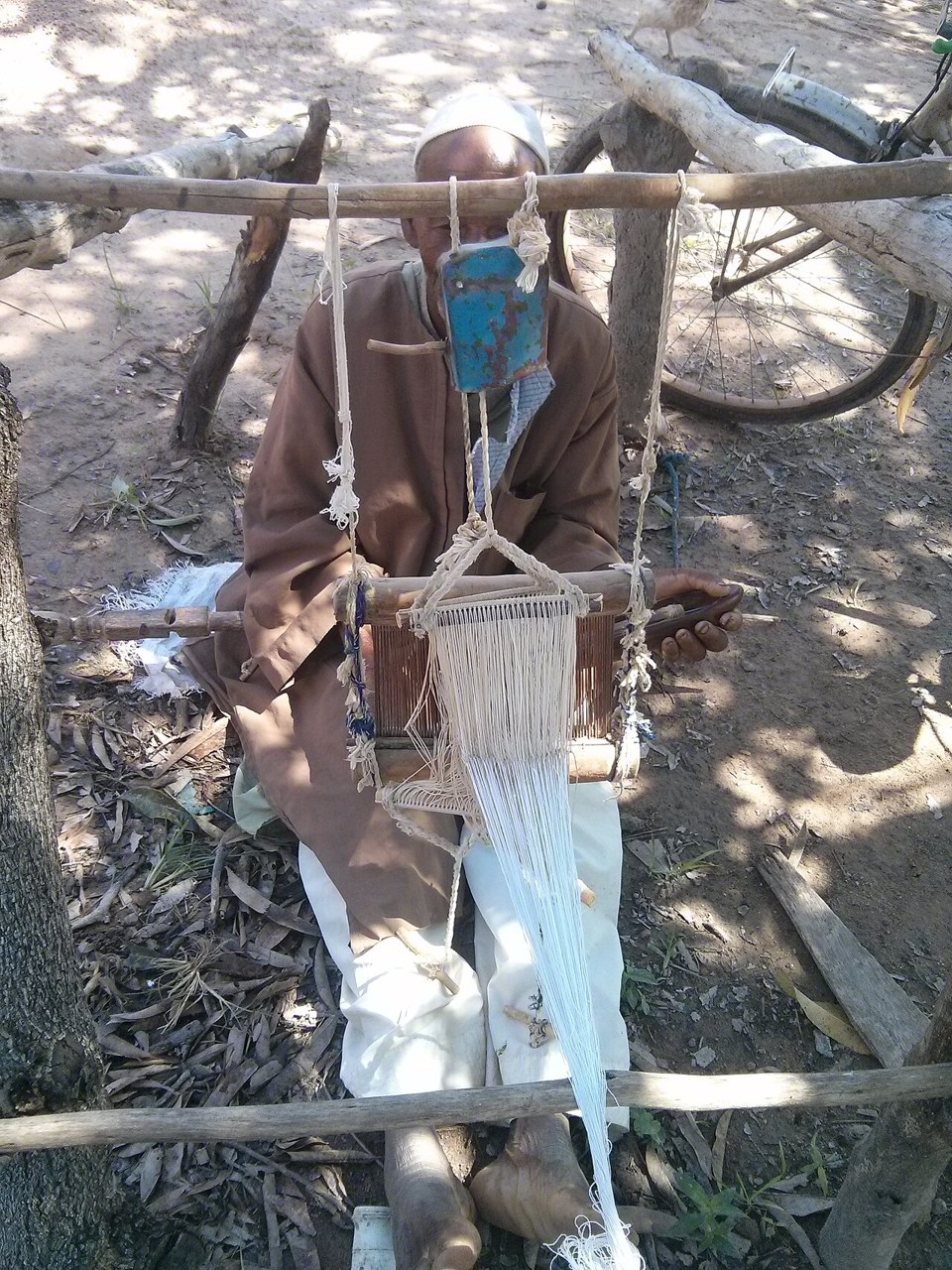 A weaver seated at a narrow handloom with white cotton threads